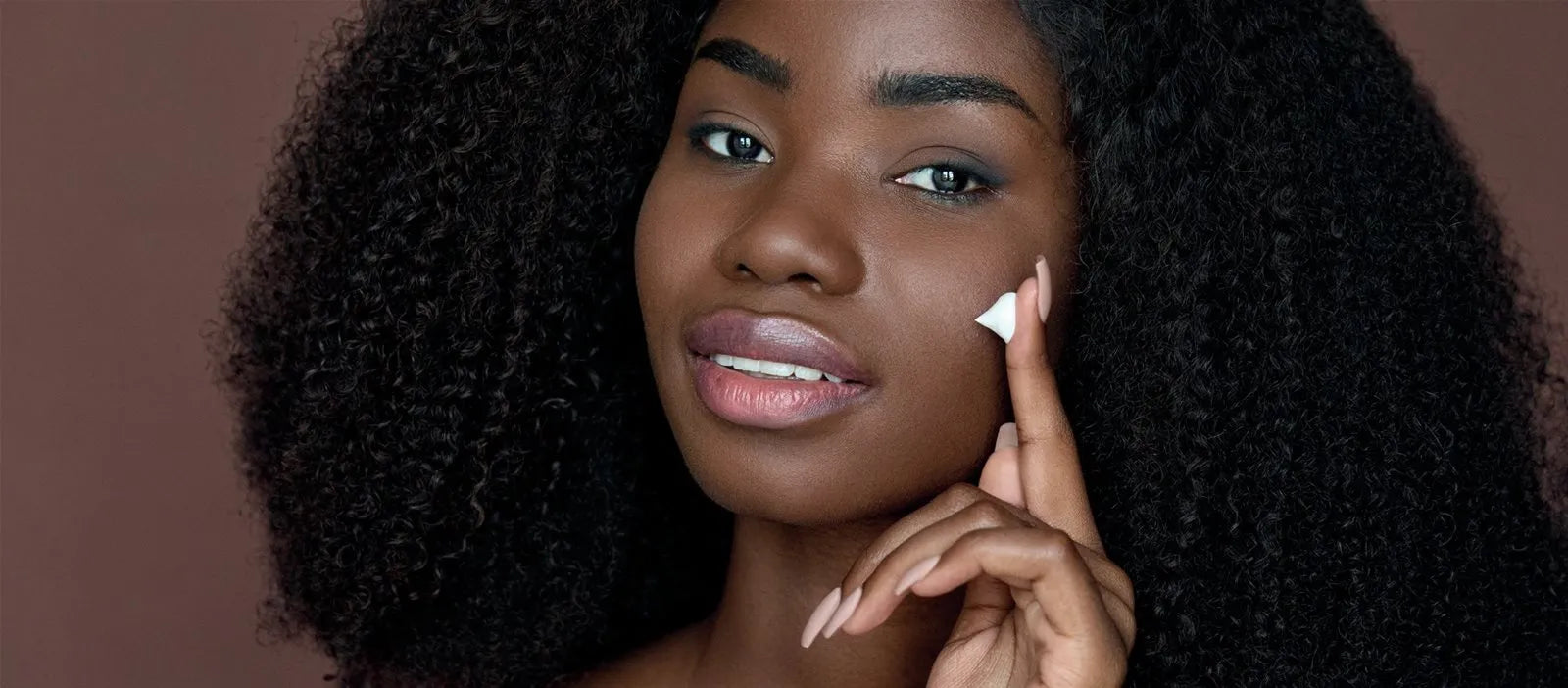 Woman with curly hair applying lip balm showing glossy moisturized lipsRetryClaude can make mistakes. Please double-check responses.