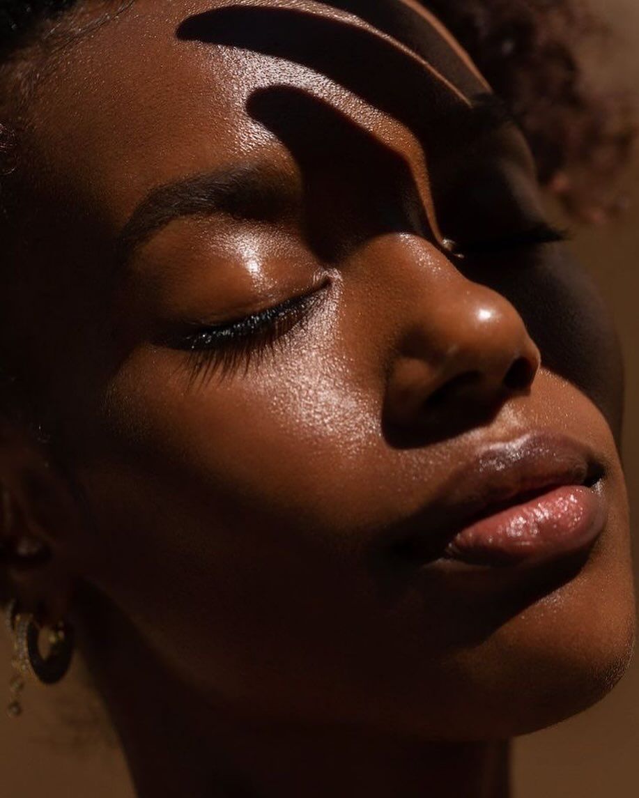 A person in a yellow outfit lies on a mustard blanket in a field of purple flowers, arms raised.