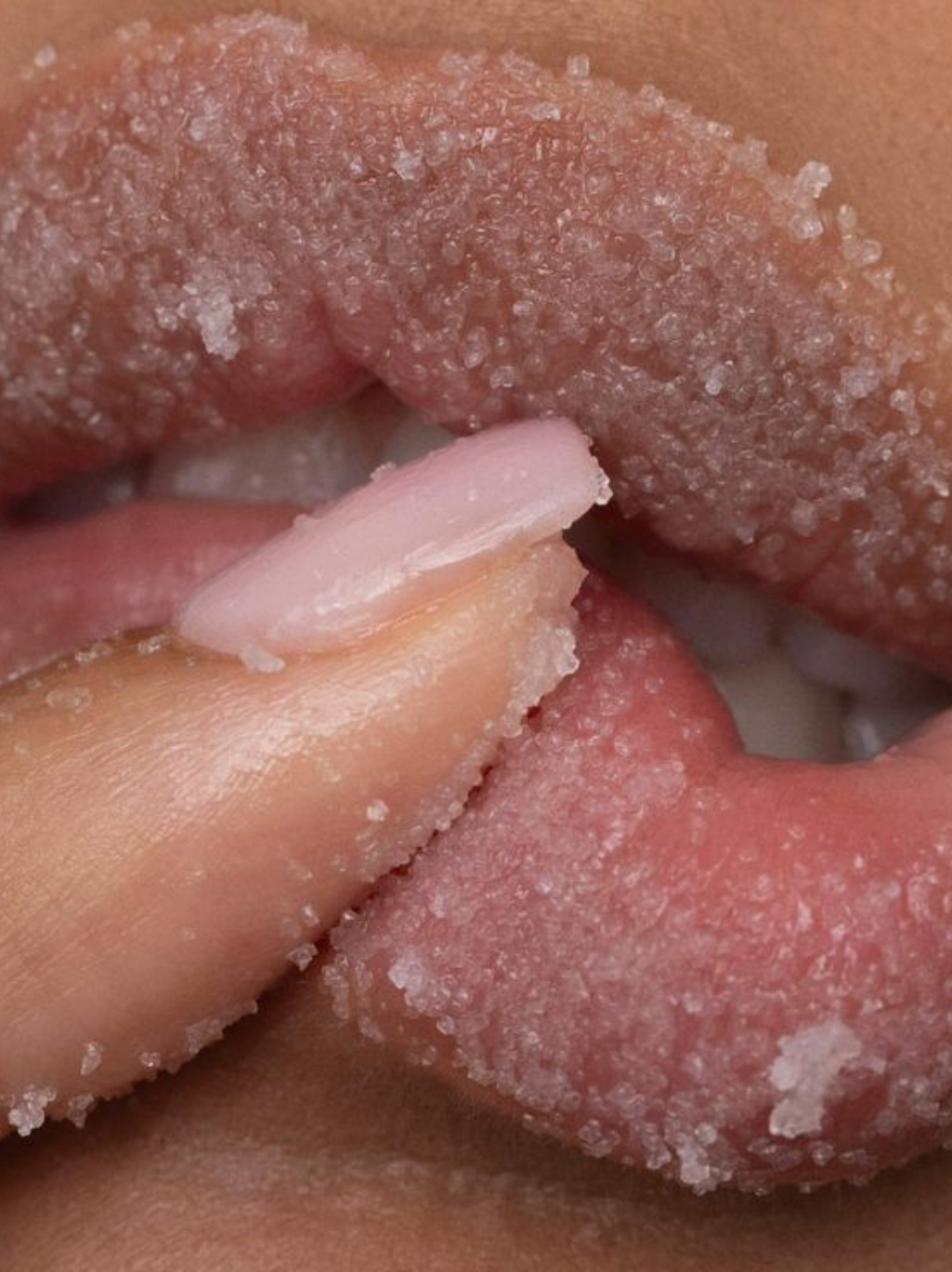 A person with dark skin applies a nude lipstick to their lips, with long dark hair visible.