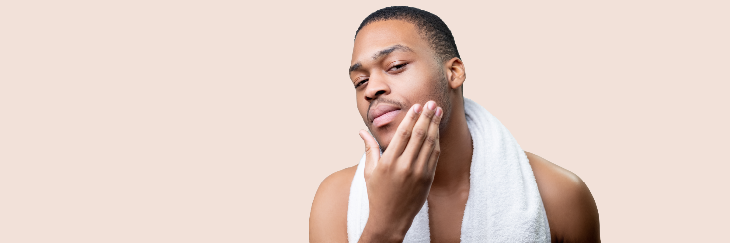 A person with a white towel around their neck touches their face, against a beige background.